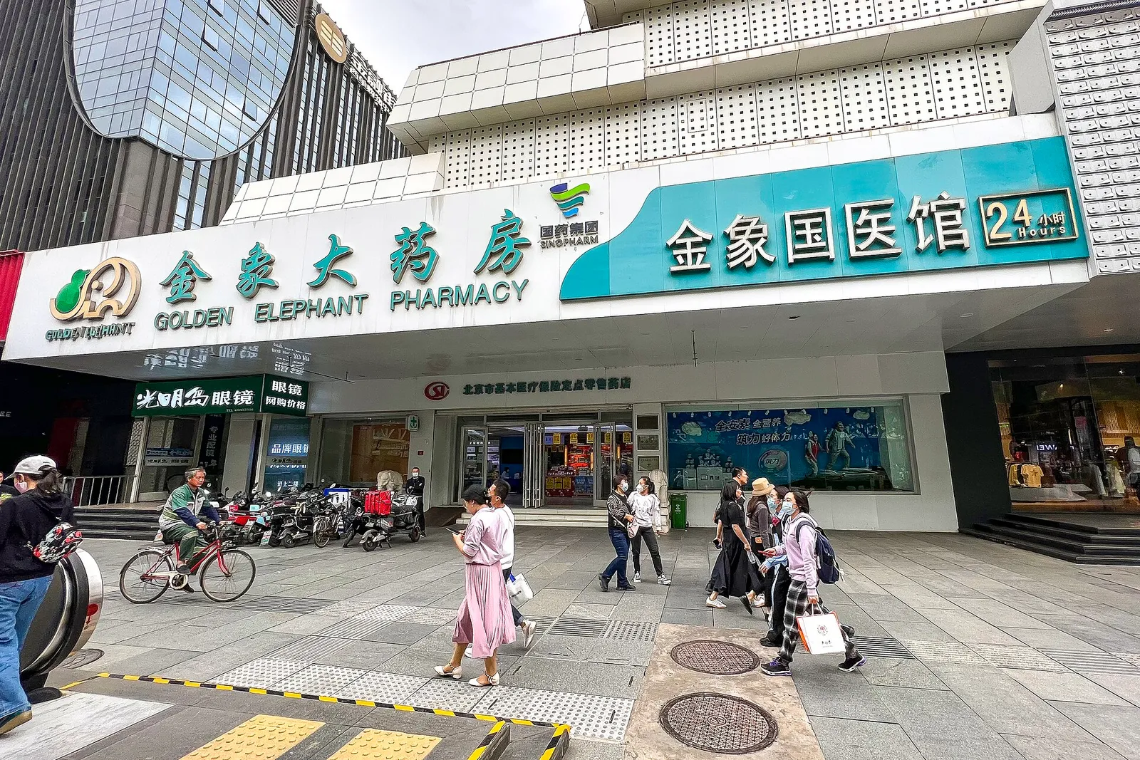 The bilingual storefront of a Golden Elephant Pharmacy branch in Beijing, with pedestrians passing on the sidewalk