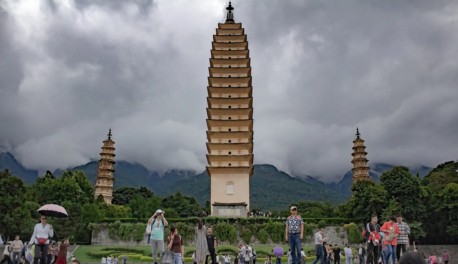 The Three Pagodas of Dali standing before the forested wall of the Cangshan mountains under clear sky