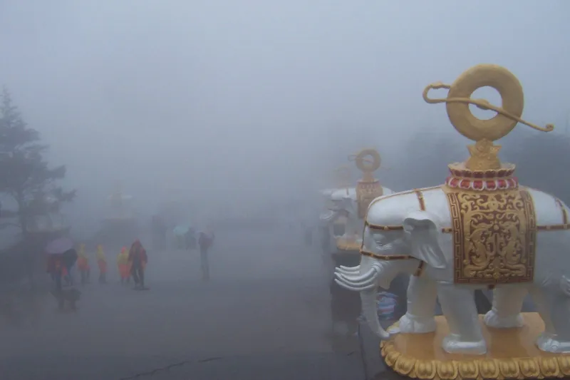 The golden ten-direction statue of Puxian at the Golden Summit of Mount Emei, rising above drifting clouds