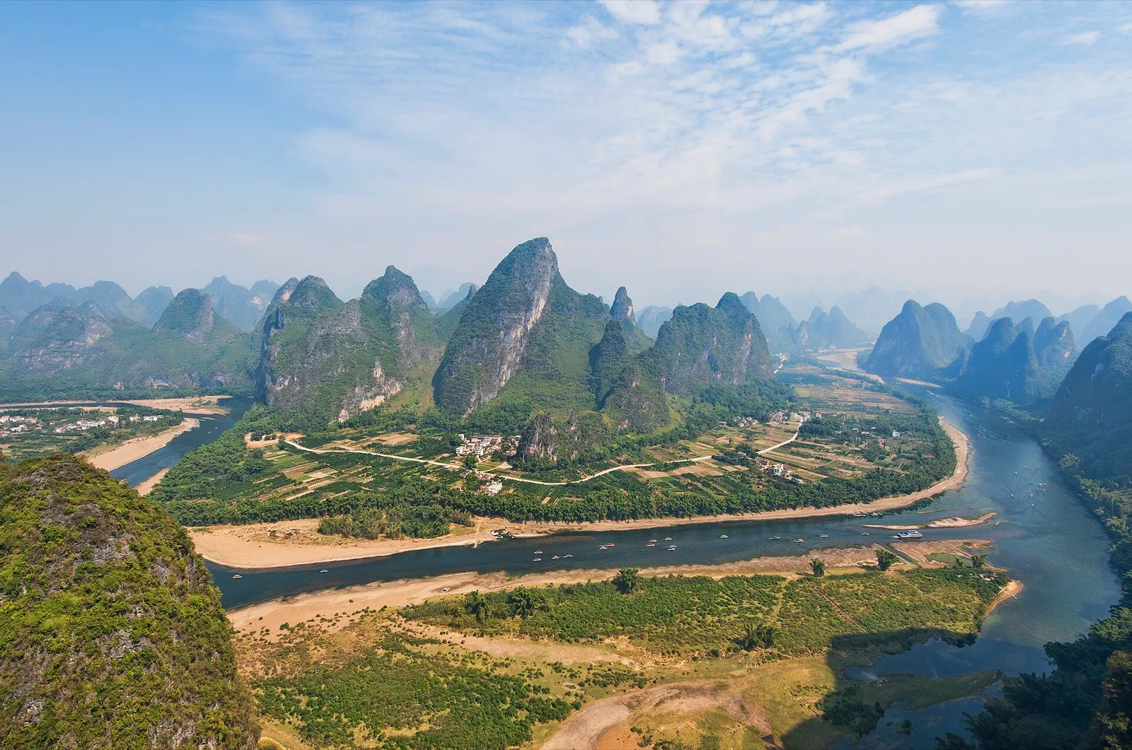 Limestone karst peaks rising from the Li River at first light, with a bamboo raft crossing the foreground
