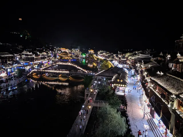 Aerial night view of Fenghuang Ancient Town, its stilt houses and rainbow bridge lit along the Tuojiang River