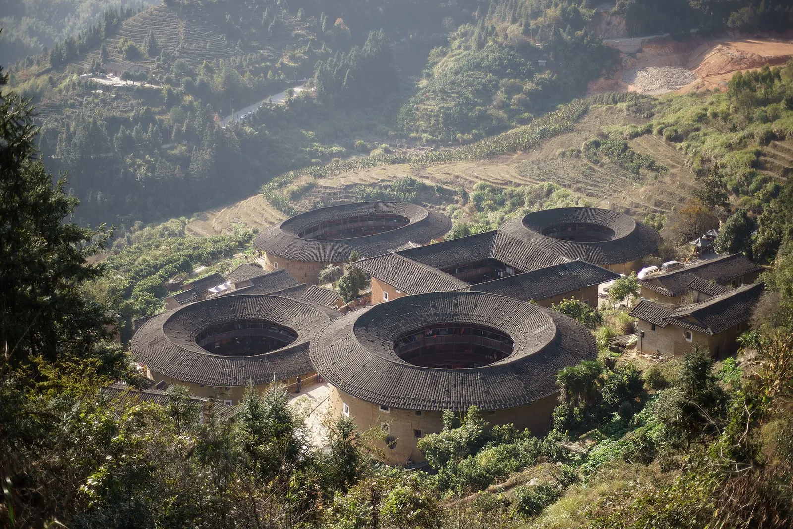 The Tianluokeng tulou cluster of earthen roundhouses seen from the hillside viewpoint amid green terraced hills in Fujian