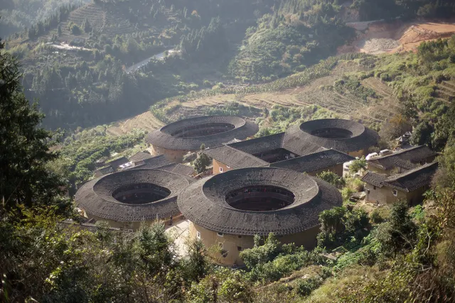 The Tianluokeng tulou cluster of earthen roundhouses seen from the hillside viewpoint amid green terraced hills in Fujian