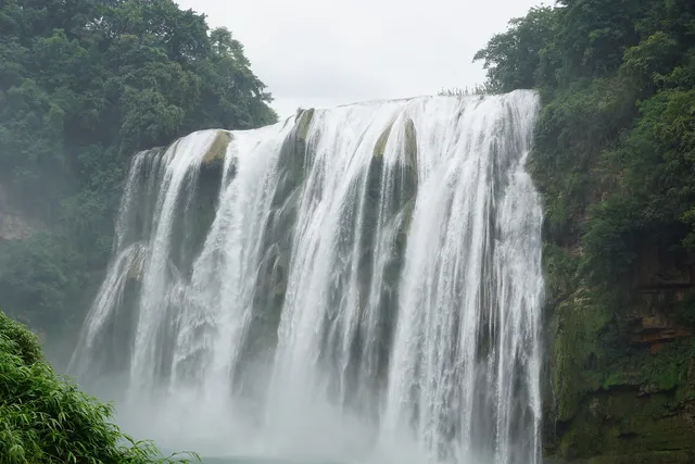 Huangguoshu Waterfall in Guizhou pouring over a wide curtain of rock surrounded by dense green forest