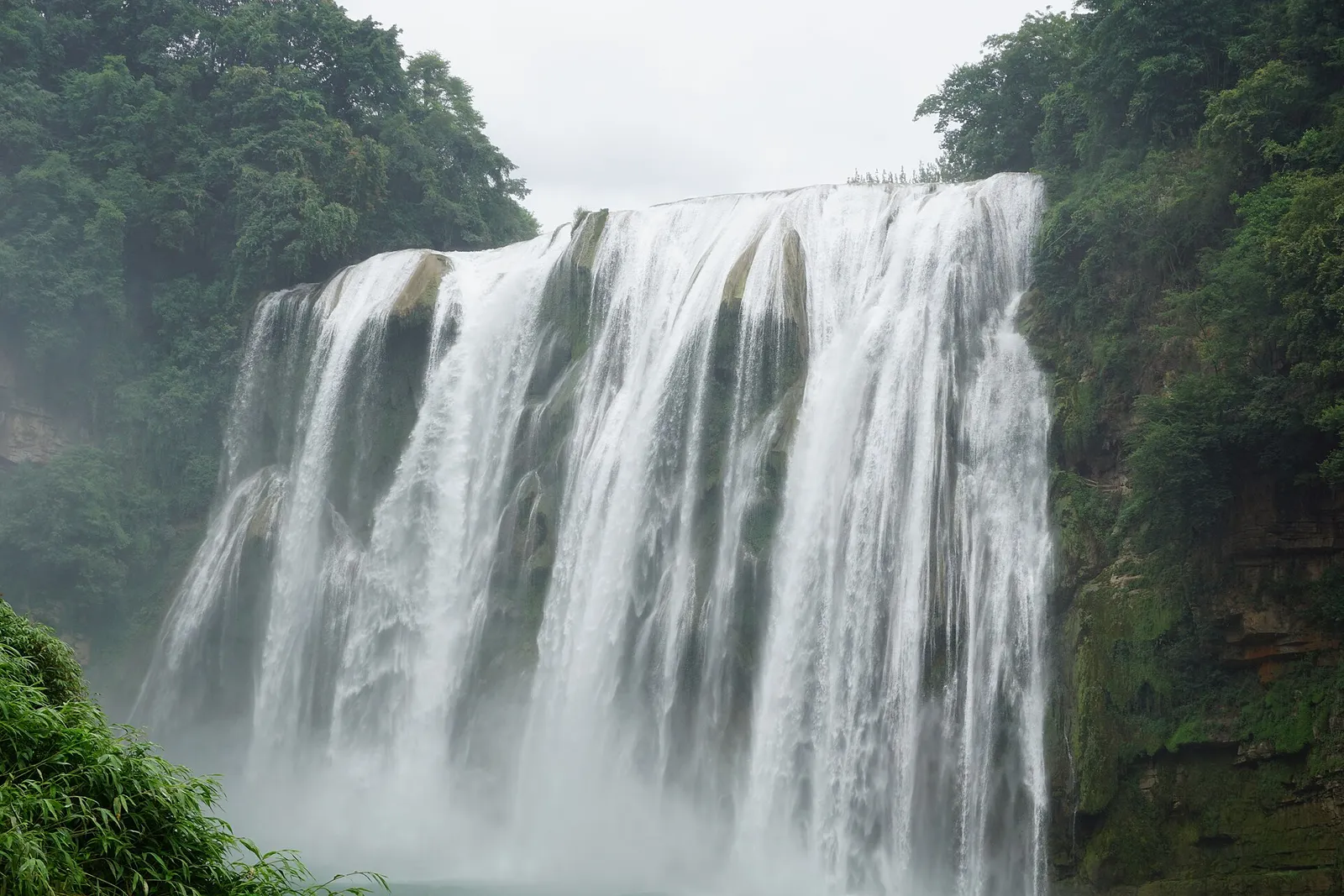 Huangguoshu Waterfall in Guizhou pouring over a wide curtain of rock surrounded by dense green forest